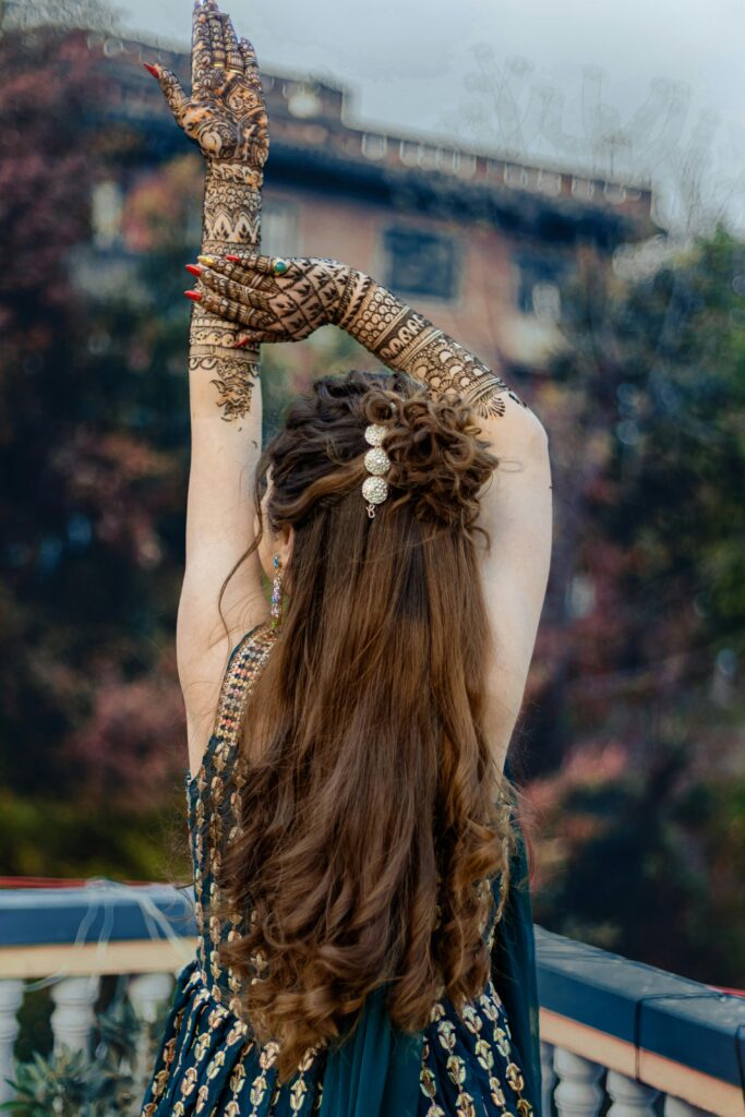 Woman with intricate mehendi on balcony, displaying back view and long curly hair.